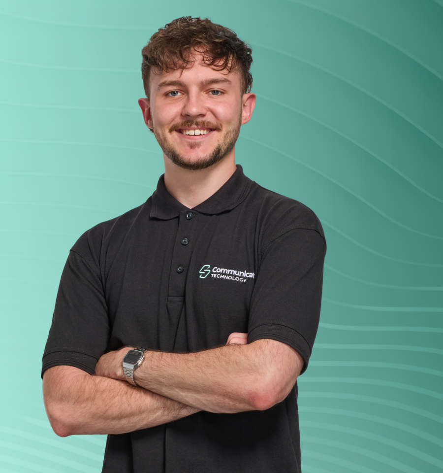 Smiling man with curly hair in black polo shirt with technology company logo, arms crossed.