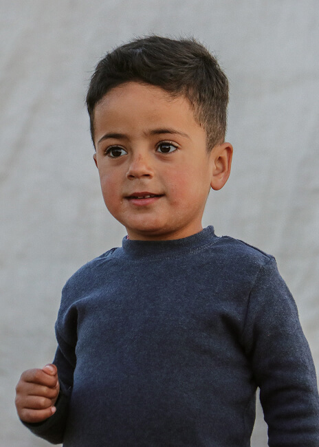 Young boy in a navy sweater standing against a tent backdrop