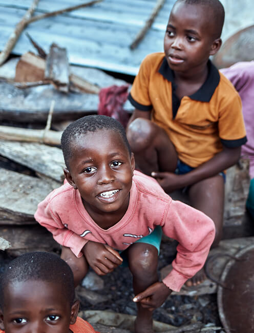 Smiling children crouched together near a wooden structure