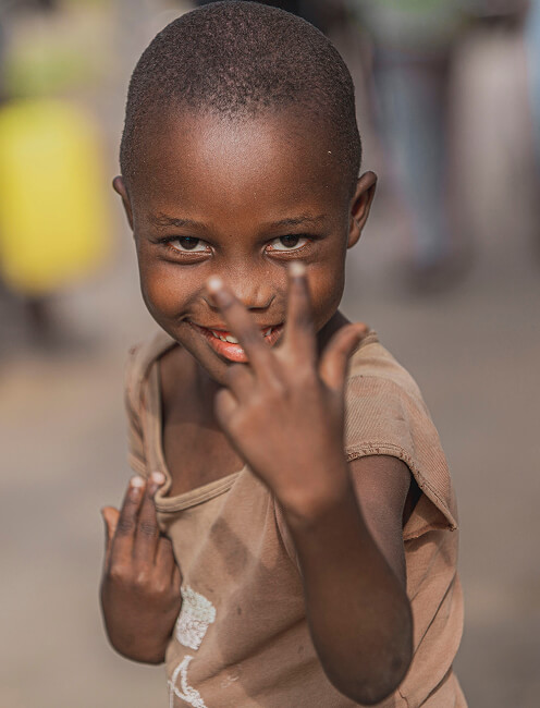 Young child making a peace sign at the camera outdoors