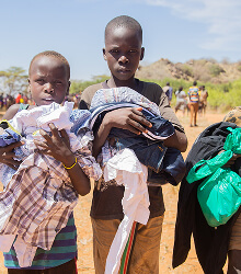 Children carrying donated clothing along a dirt path