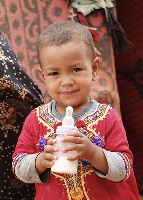 Toddler in traditional embroidered clothing holding a milk bottle