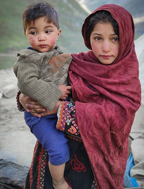 Young girl in a headscarf holding a toddler outdoors