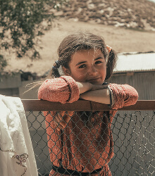 Girl leaning on a fence rail outside a shelter