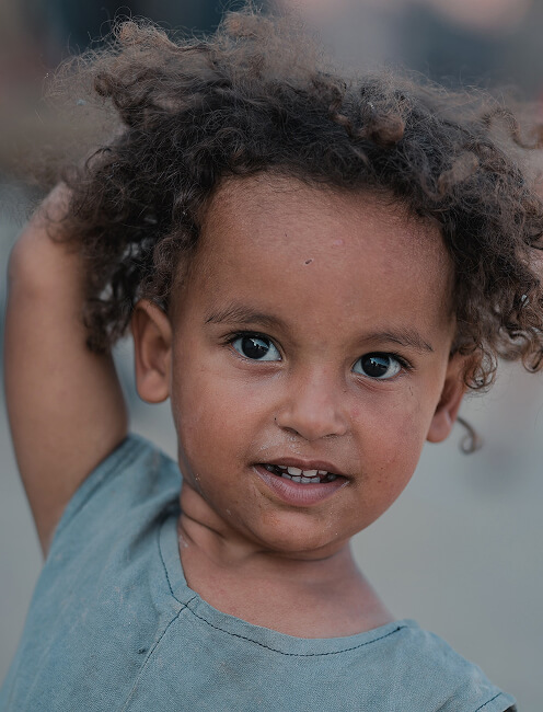 Close-up of a curly-haired toddler smiling outdoors