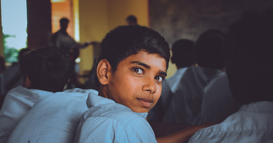 Boy in school uniform looking back in a classroom full of students