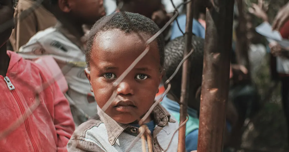 Young boy looking through a wire fence at a displacement camp