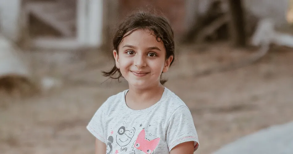 Smiling young girl standing outdoors, supported by Karuna's child recovery programs