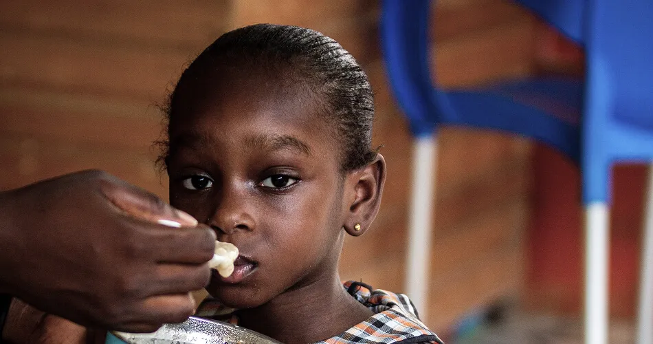 "Young girl being fed nutritious food by caregiver as part of child nutrition program