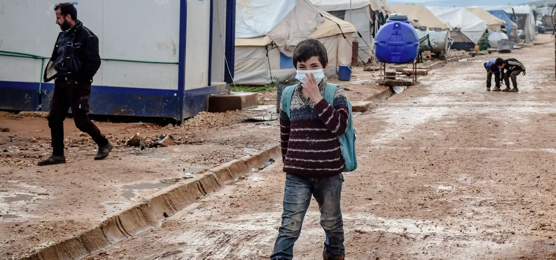 Boy with backpack walking to school in a conflict-zone refugee camp