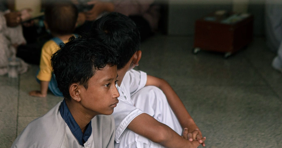 Boys sitting together indoors, holding hands in a shelter setting