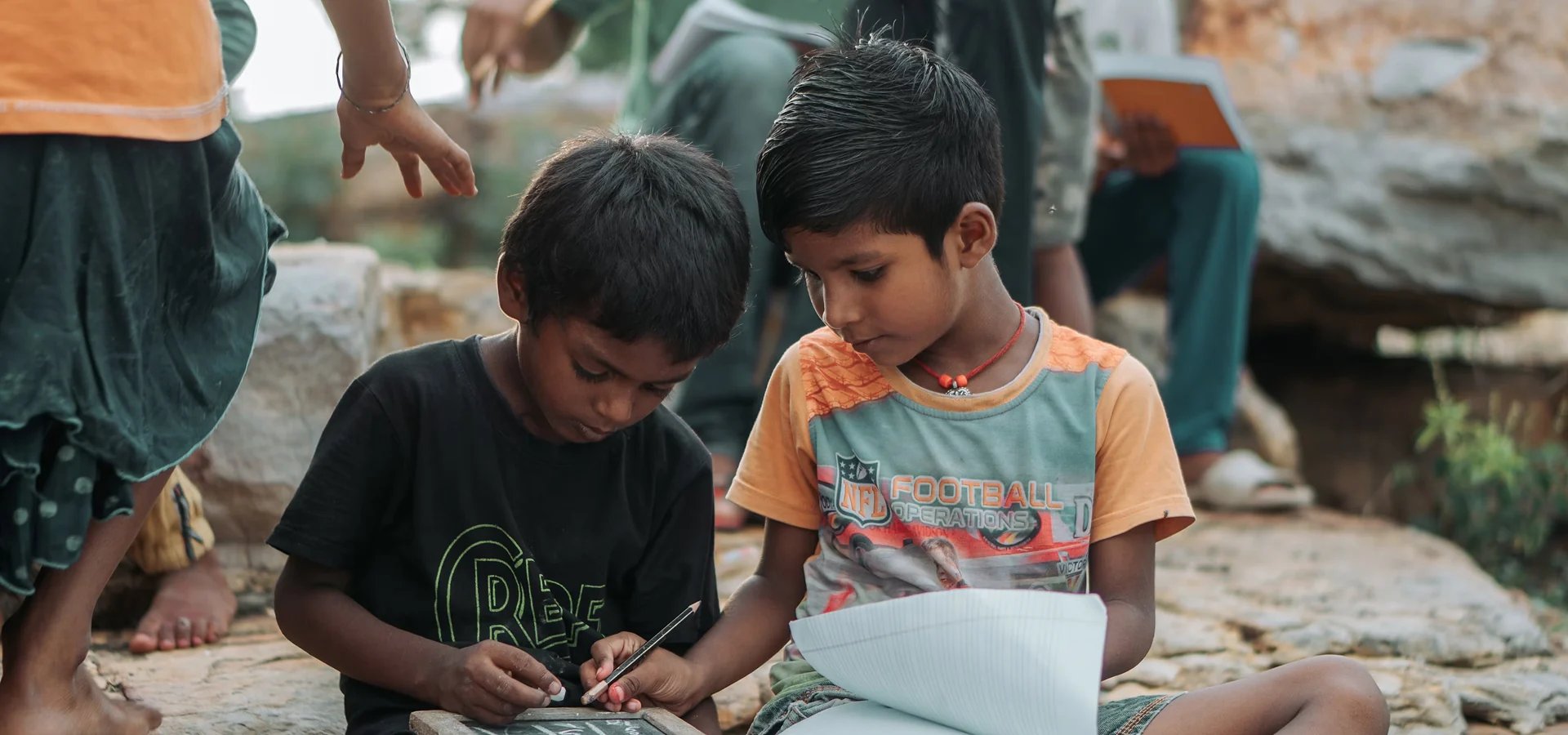 Two boys writing and reading together outdoors as part of Karuna's education program