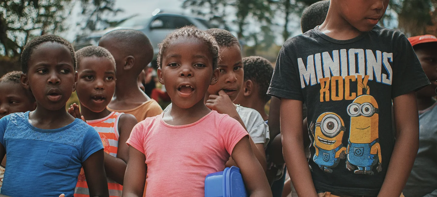 Group of excited children waiting near a schoolhouse for book distribution