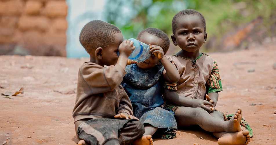 Young children sharing water while sitting together outdoors