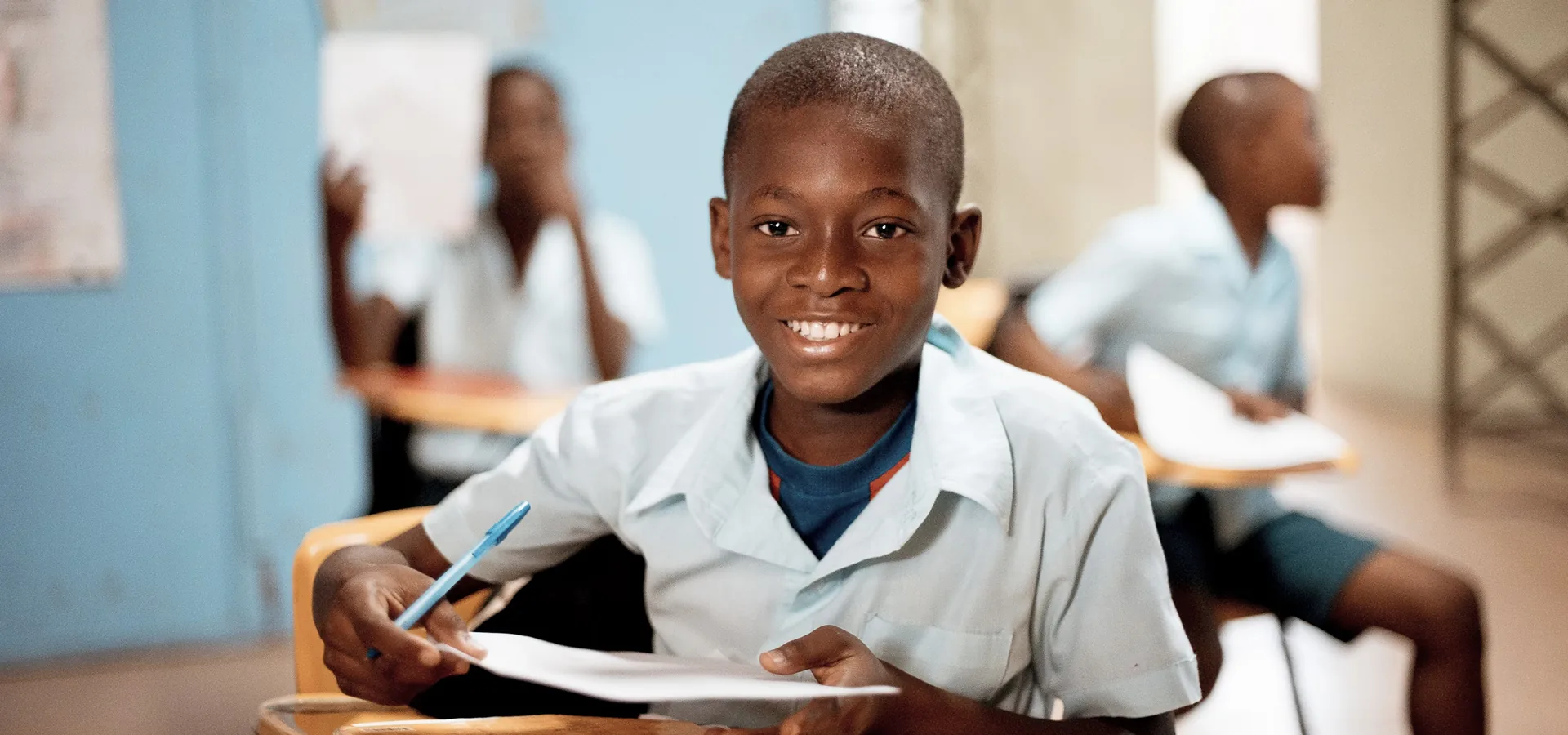 Smiling boy in school uniform writing at his classroom desk