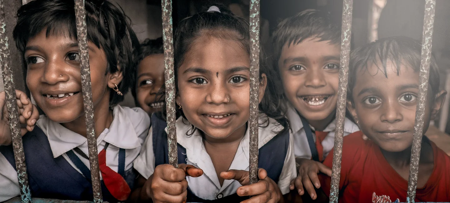 Smiling children in school uniforms peeking through metal bars