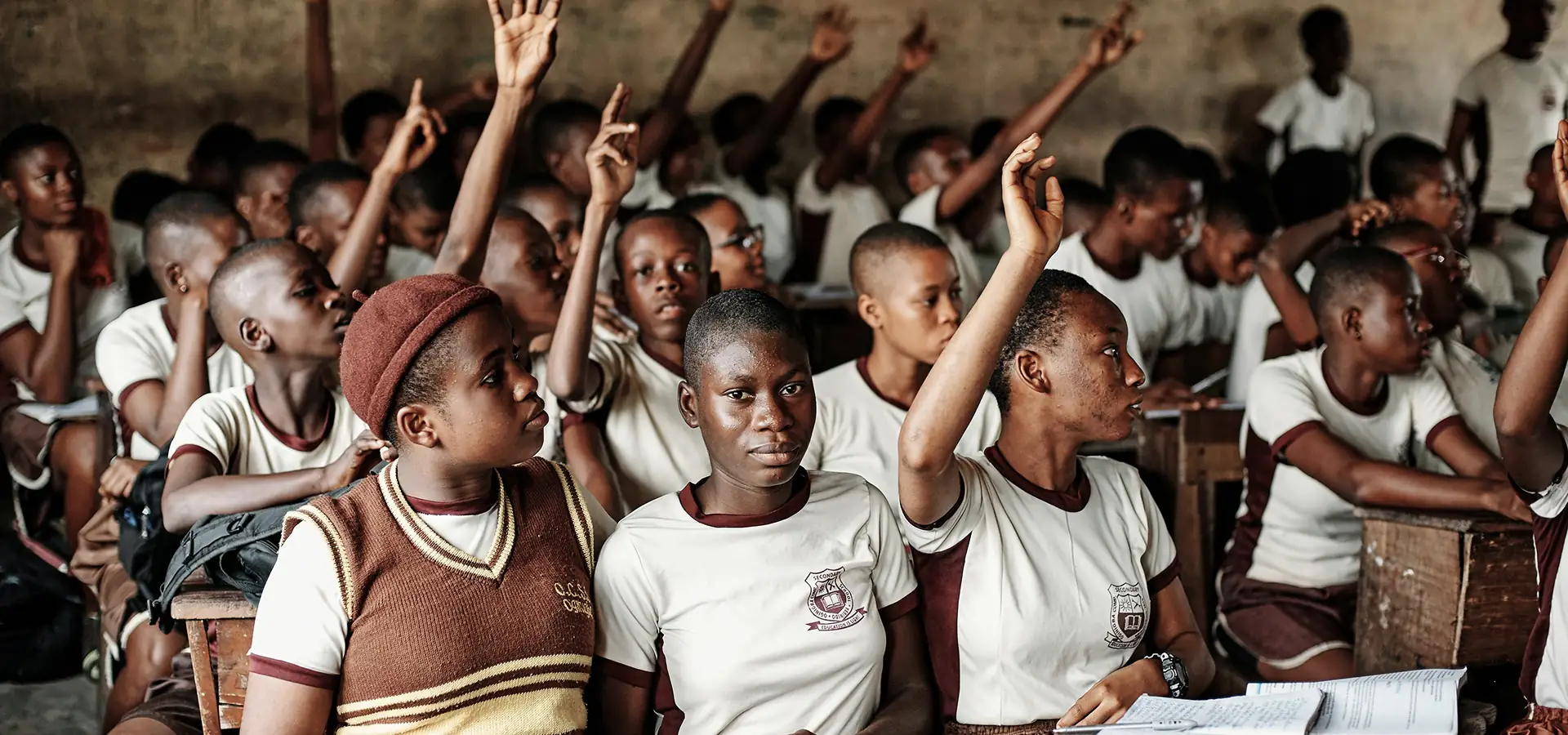 Students in school uniforms raising hands in a full classroom