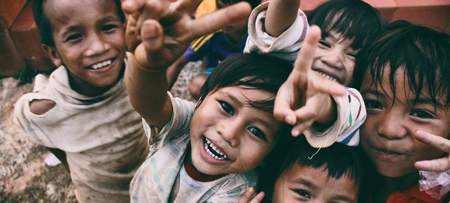 Smiling children making peace signs and reaching toward the camera outdoors