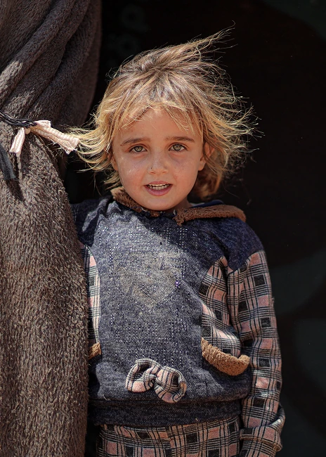 Young girl standing beside a tent flap at a displacement camp