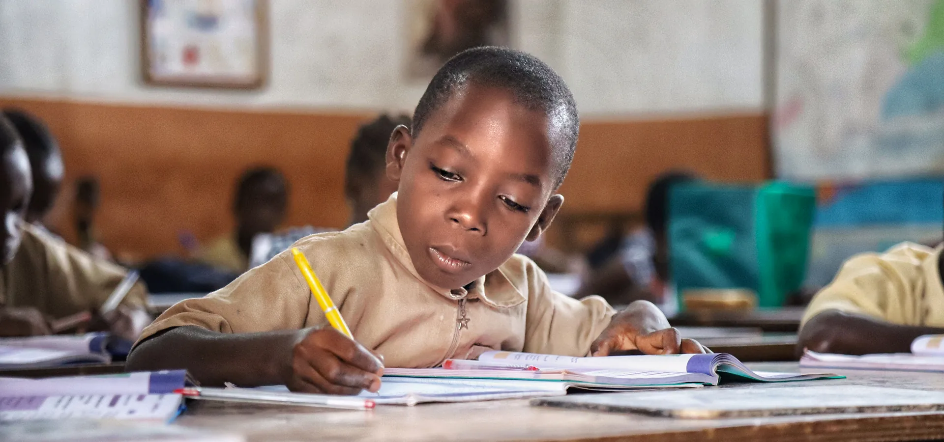 Boy in school uniform writing at his desk in an education program classroom