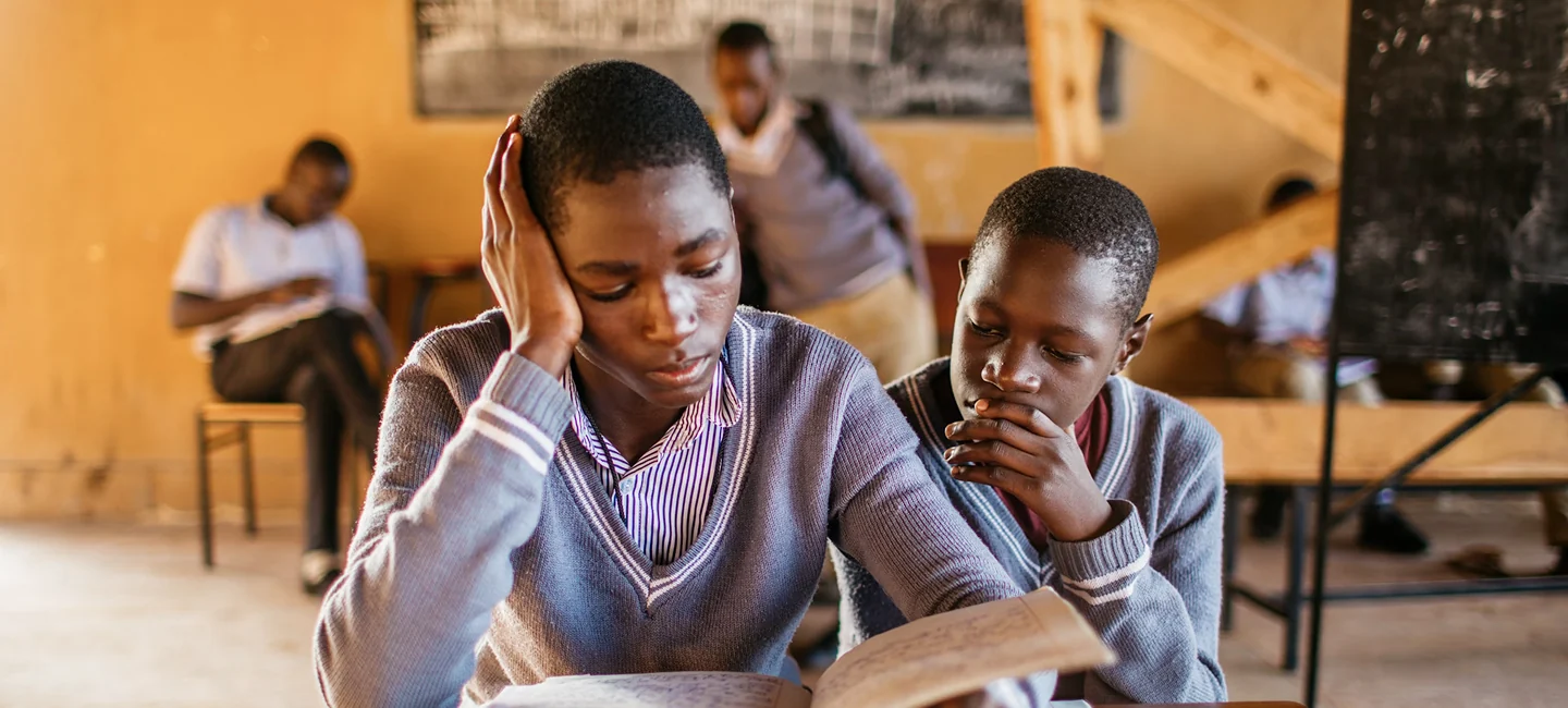 Students in school sweaters reading a textbook together in class