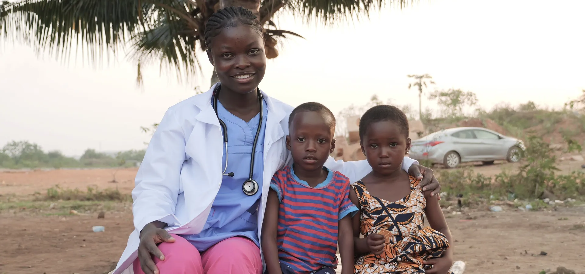 Doctor with two children outdoors at a community health program site