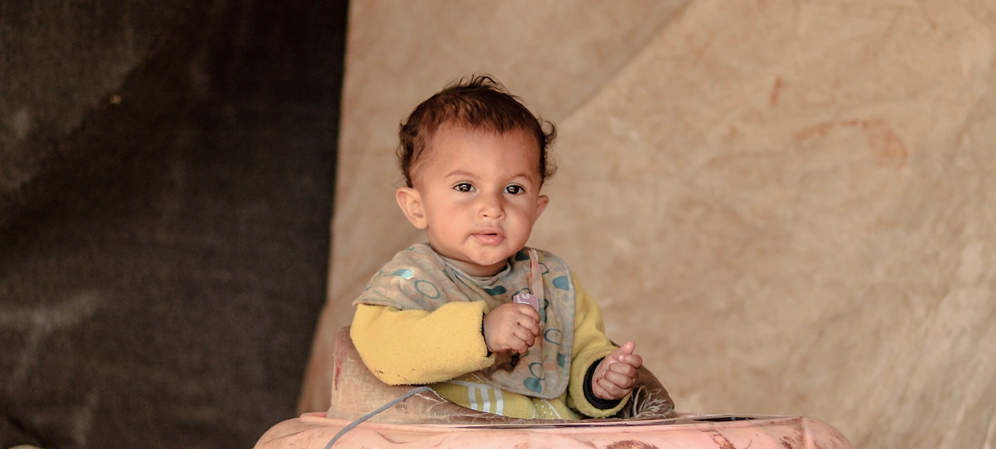Baby sitting inside a tent shelter looking at the camera