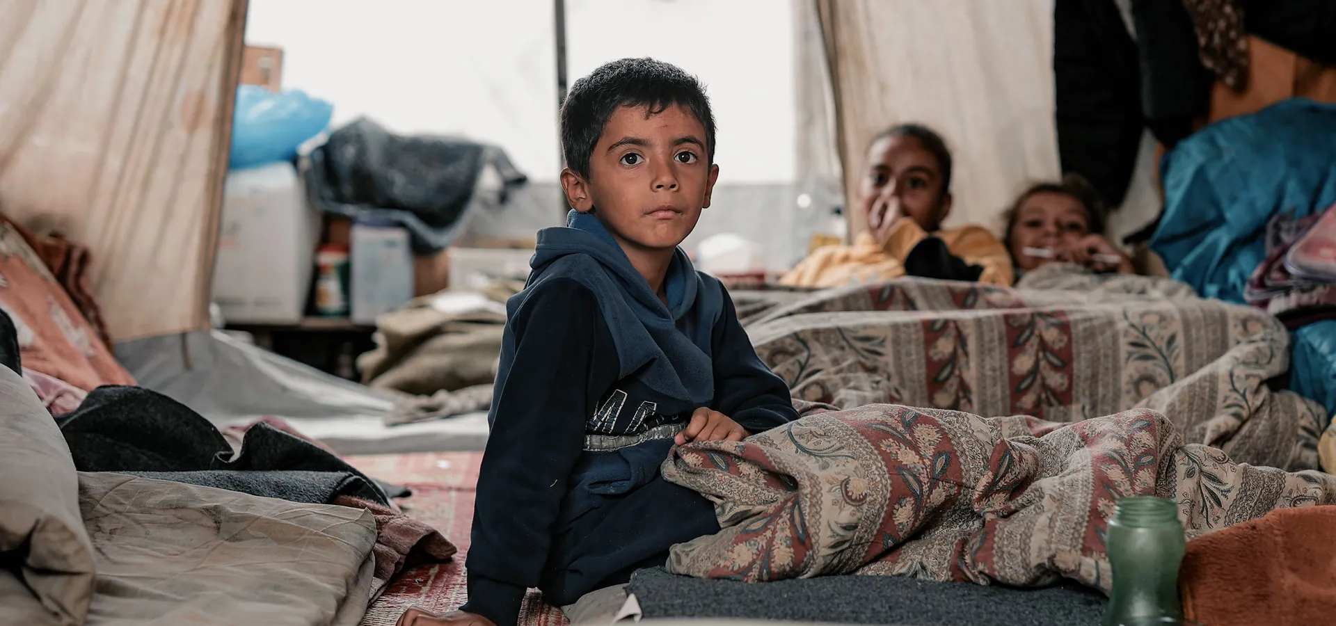 Boy sitting among bedding inside a shelter tent