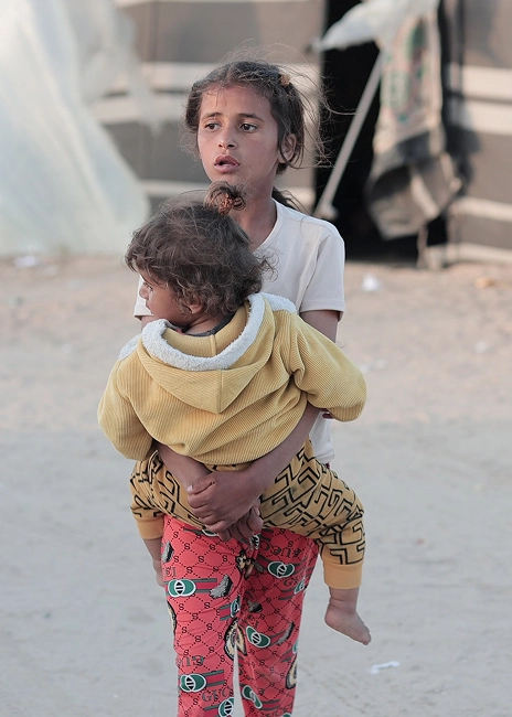 Girl carrying a toddler outside tents at a displacement camp