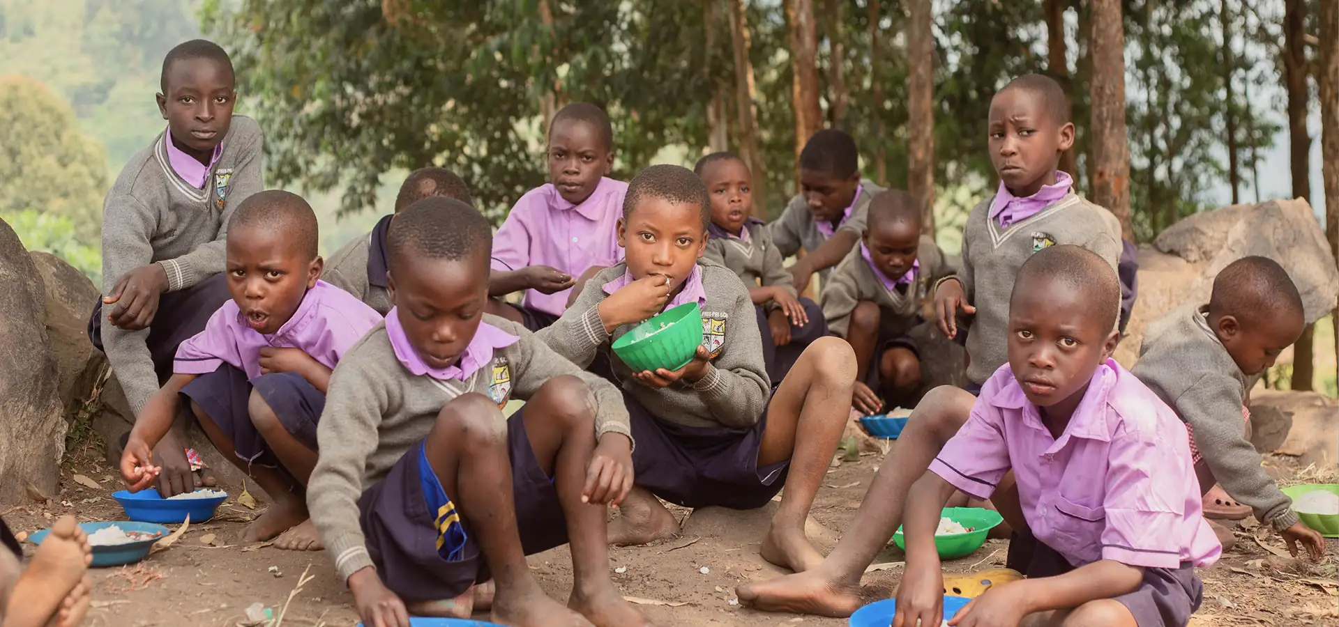Students in school uniforms eating meals together outdoors as part of a food program