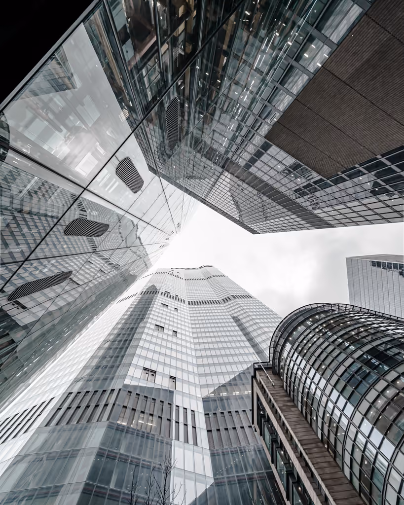 Upward view of multiple modern glass skyscrapers reflecting each other under a cloudy sky.