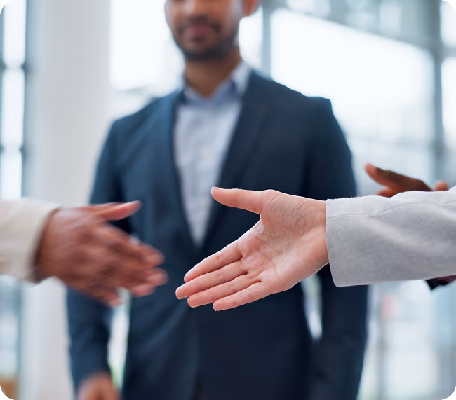 Two people reaching out to shake hands with a blurred man in a suit in the background.