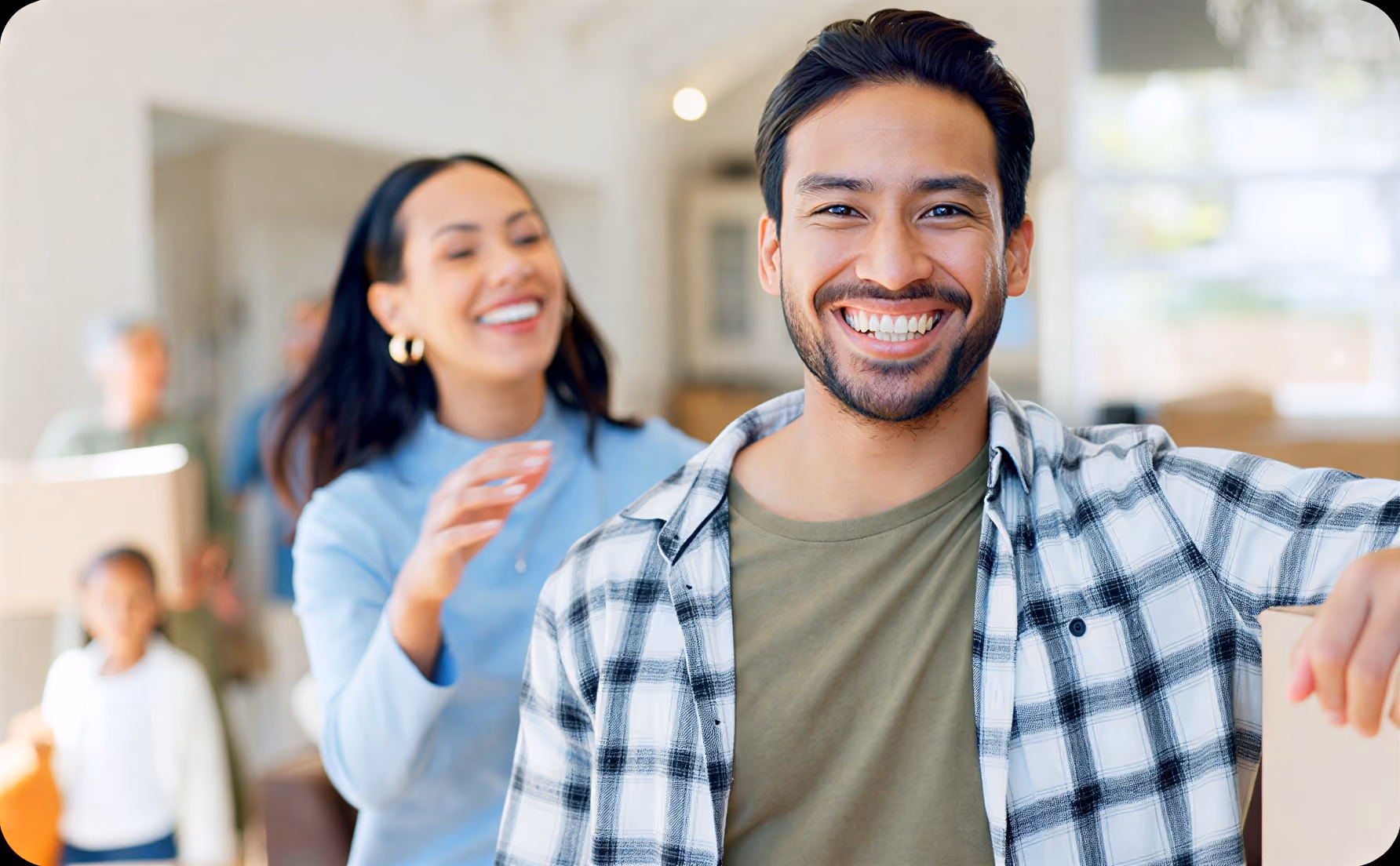 Smiling young man holding a box with a happy woman and family blurred in the background.