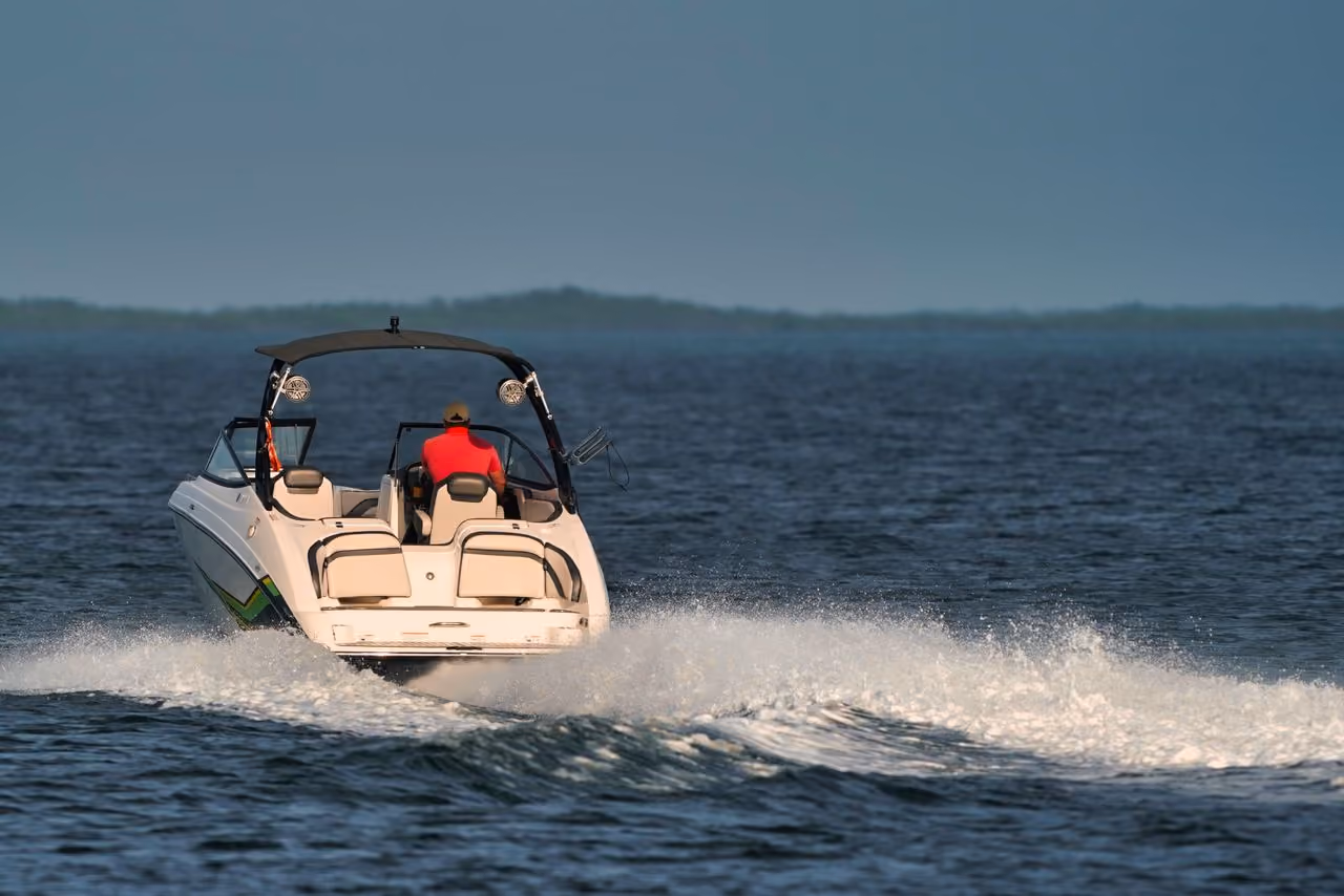 Person in red shirt driving white motorboat on water creating a wake with horizon in background.