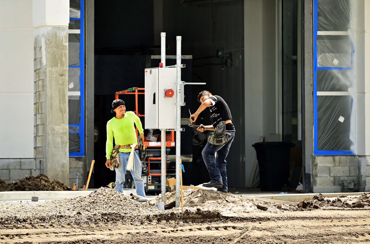 Two construction workers installing electrical control box at a building site under construction.