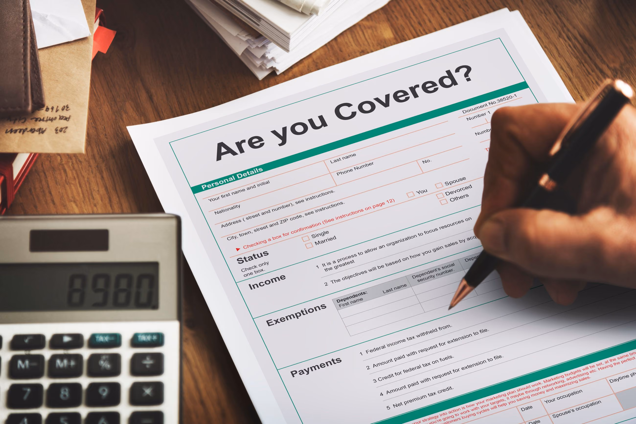 Hand holding pen filling out an insurance form titled 'Are you Covered?' on a wooden desk with calculator.
