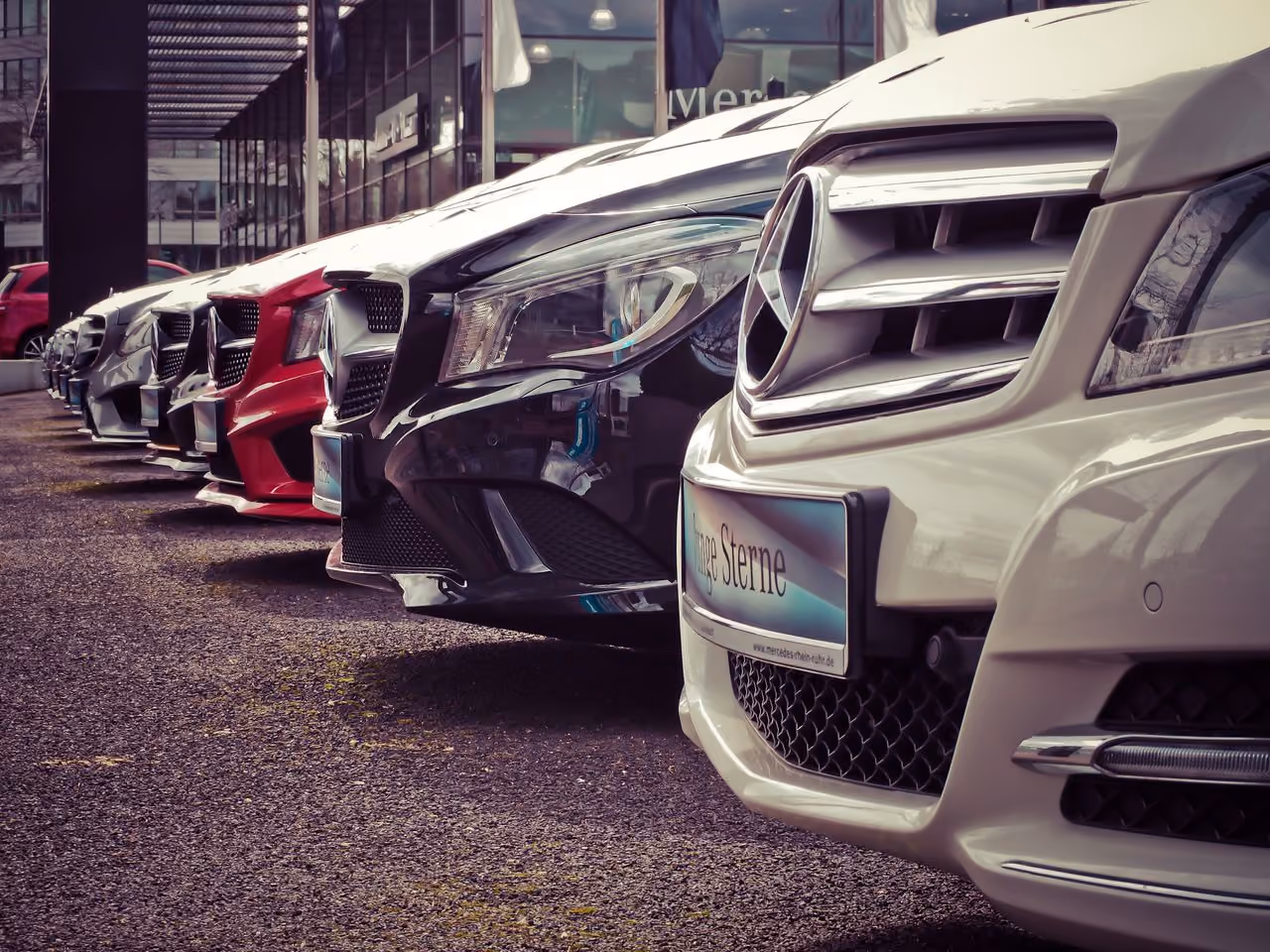 Row of Mercedes-Benz cars parked diagonally outdoors with close-up on their front grilles.