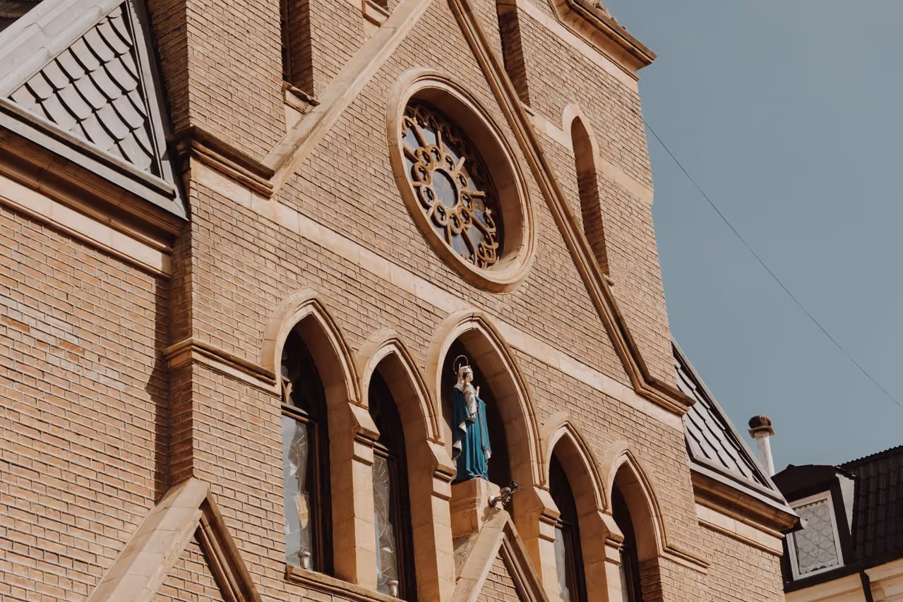 Close-up of church facade with arched windows, a statue, and a circular stained-glass window.