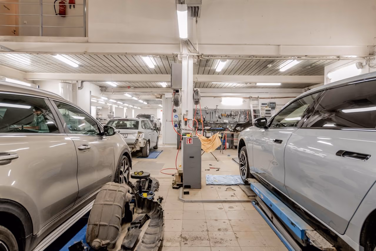 Interior of a brightly lit auto repair garage with cars and tools for vehicle maintenance.