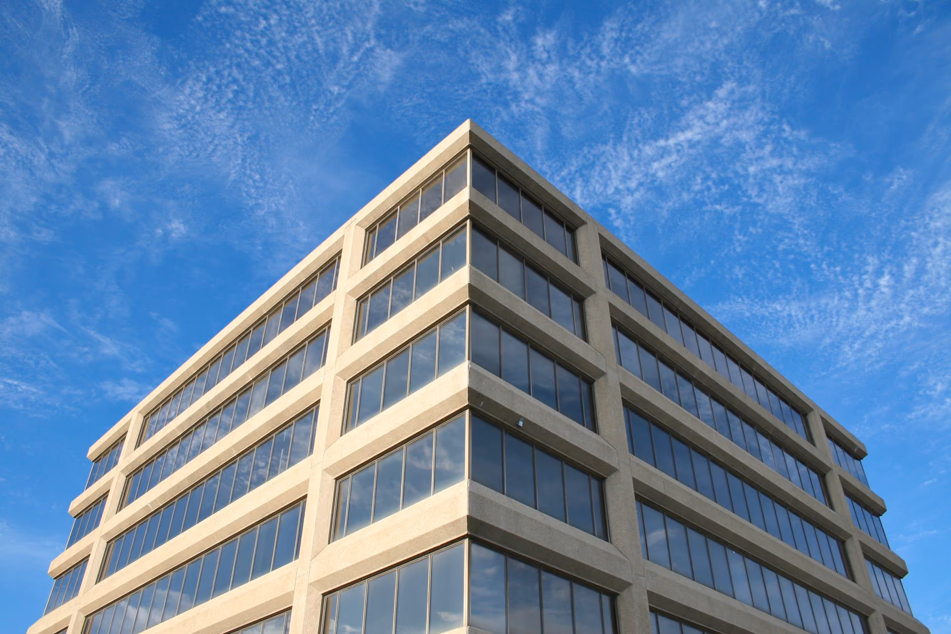 Corner view of modern office building with reflective windows under a blue sky with wispy clouds.