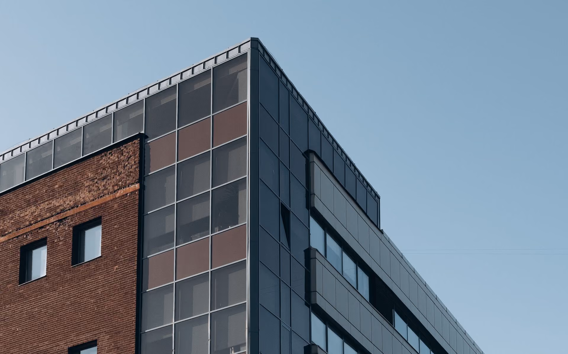 Modern commercial building corner with brick facade and large glass windows under clear sky.