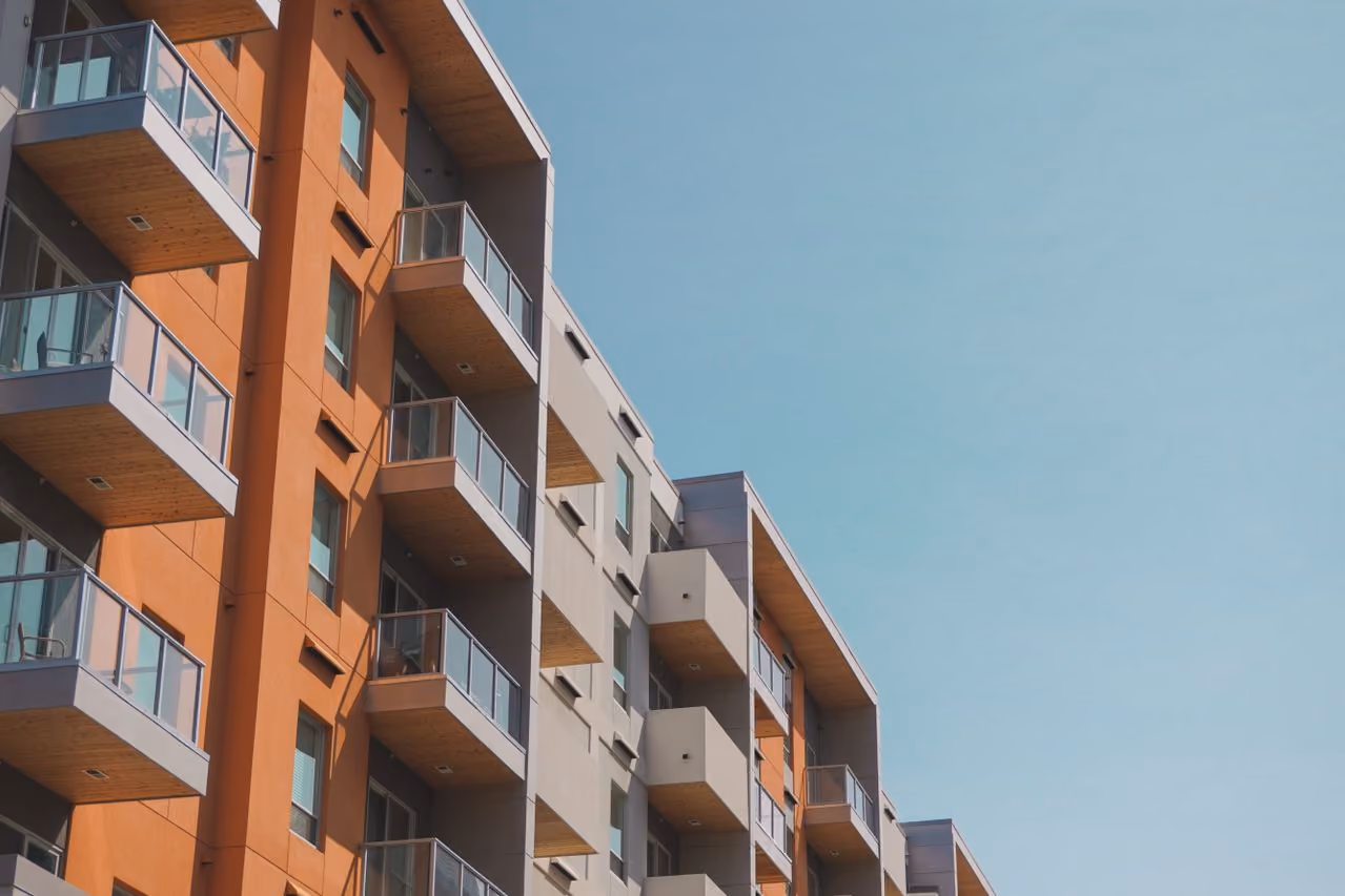 Modern apartment building with orange and gray walls and multiple balconies under a clear sky.