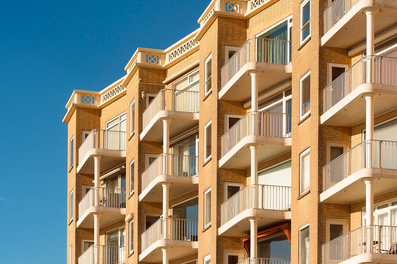 Exterior view of a modern brick apartment building with multiple balconies under a clear blue sky.