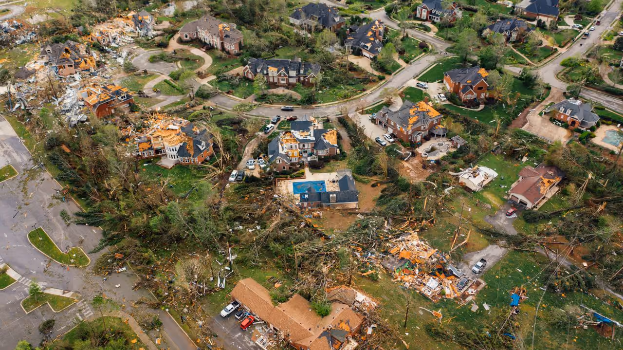 Aerial view of a neighborhood with extensive wind damage and debris strewn across yards and streets.