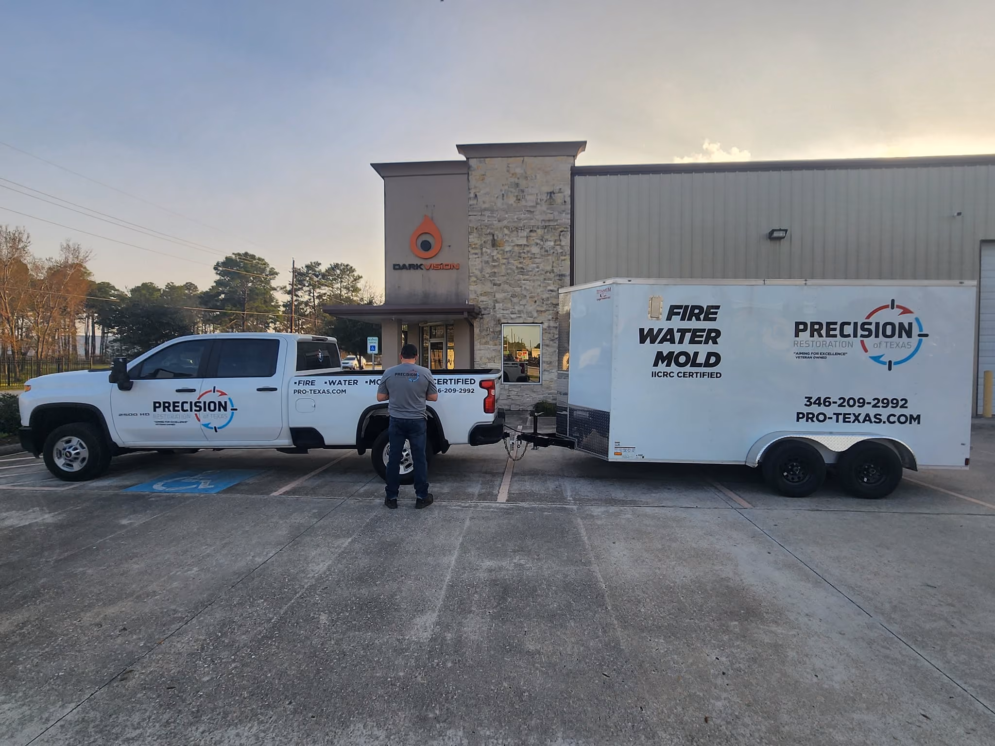 Man in Precision Restoration shirt stands by truck and trailer with fire, water, mold restoration signage.