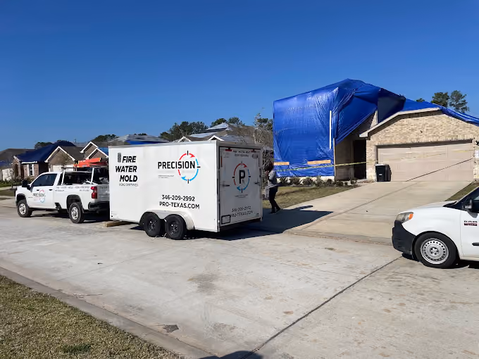 Residential houses with tarps covering roofs and Precision restoration company trucks and trailer parked on the street.