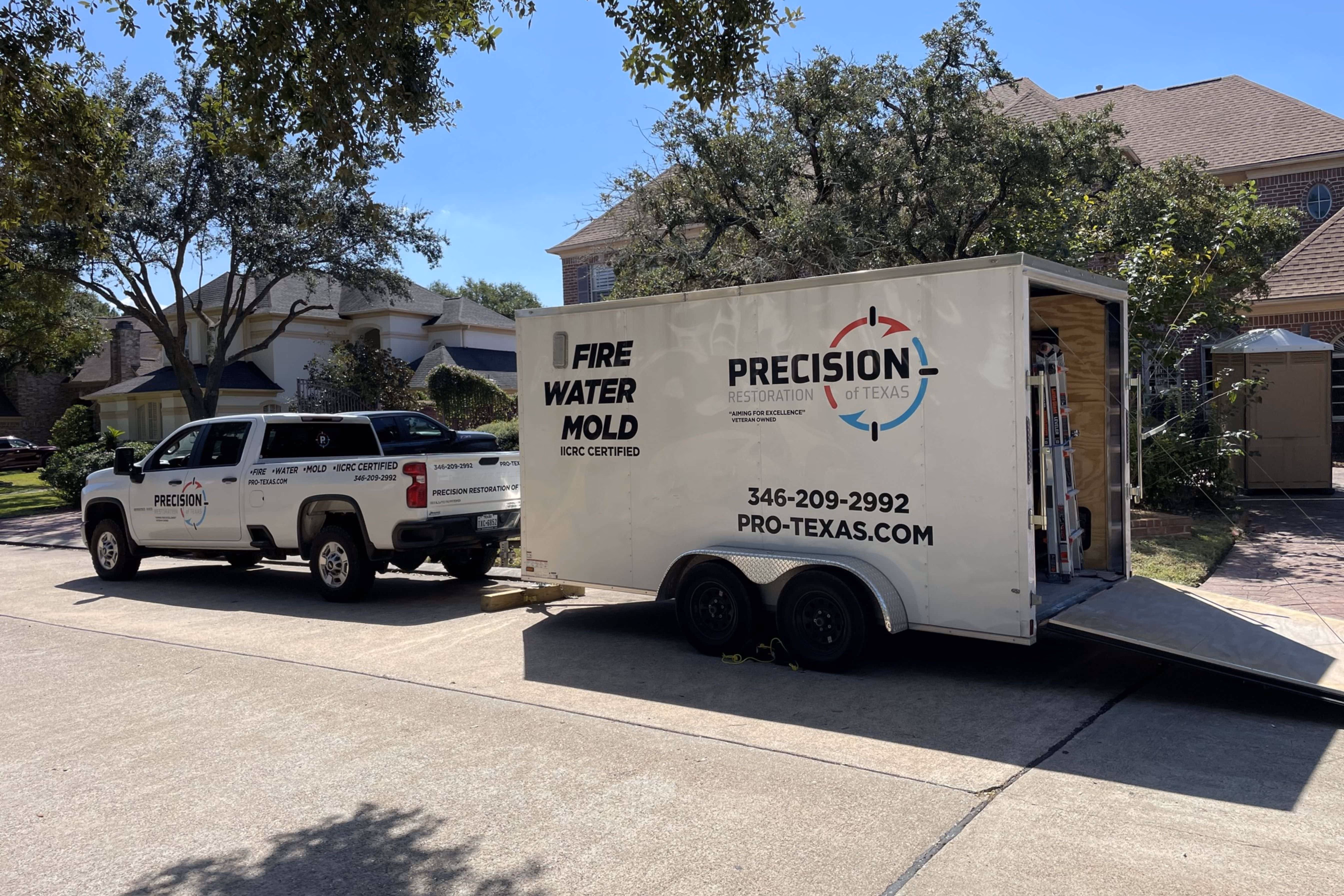 White Precision of Texas truck connected to a trailer with open ramp on a suburban street.