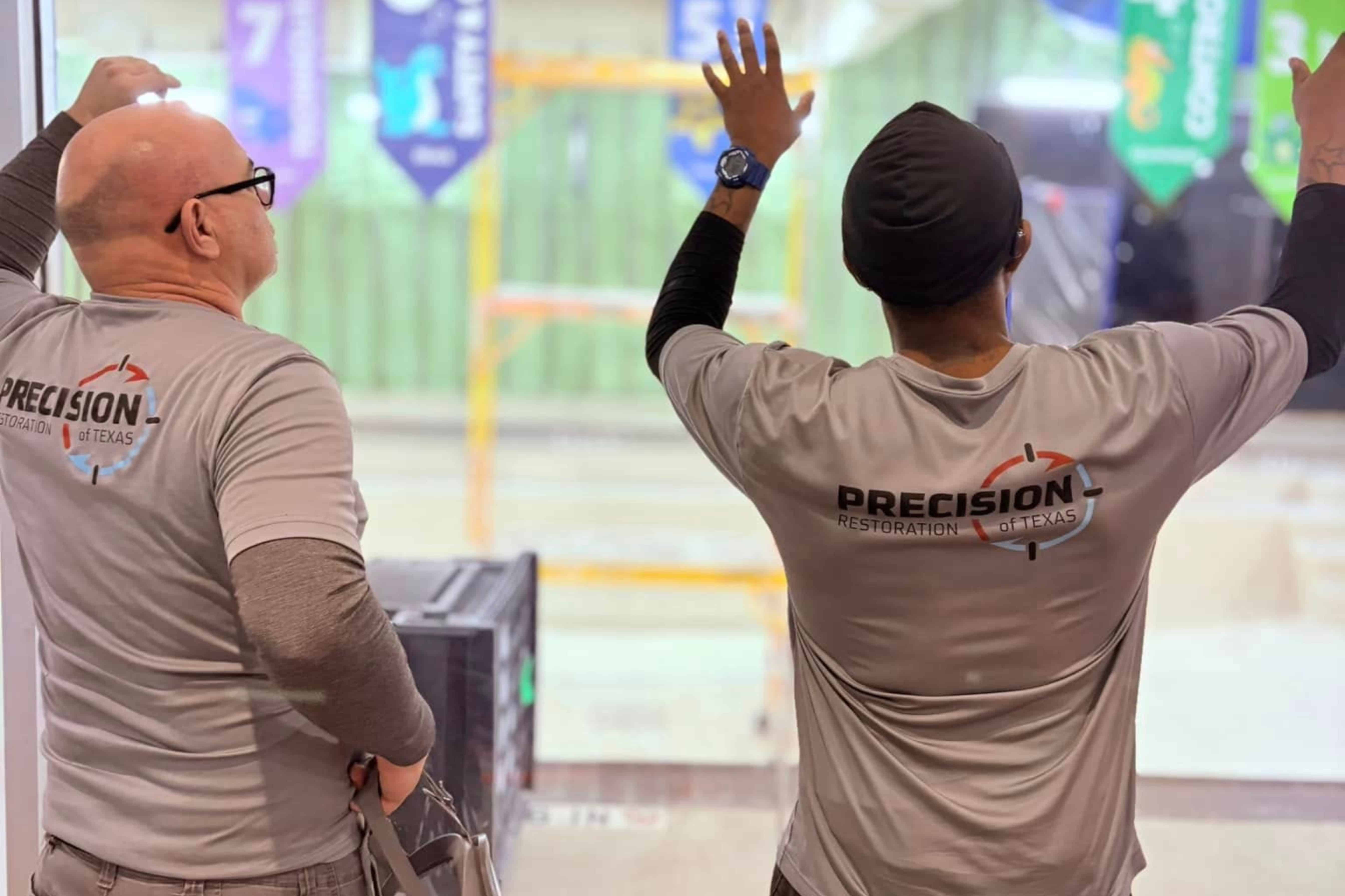 Two workers from Precision Restoration of Texas standing with arms raised inside a building under construction.