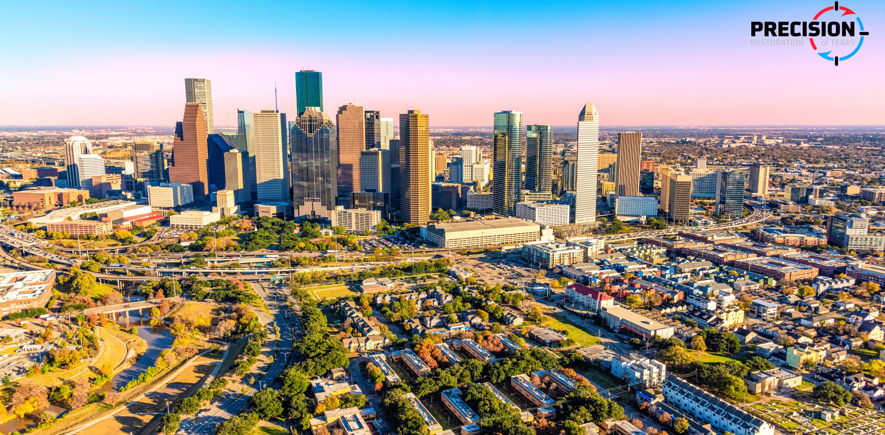 Aerial view of a city skyline with tall buildings and residential areas under a blue sky.