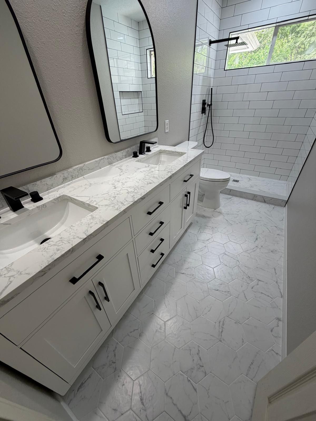 Modern bathroom with white double sink vanity, black fixtures, hexagonal floor tiles, and a walk-in shower.